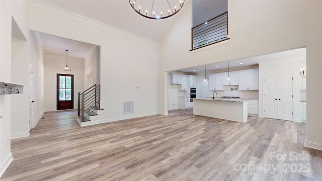 unfurnished living room featuring stairs, light wood-type flooring, visible vents, a notable chandelier, and baseboards