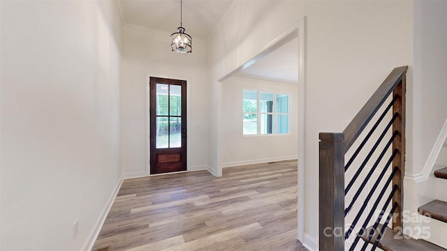 foyer entrance featuring an inviting chandelier, stairway, light wood-style flooring, and baseboards