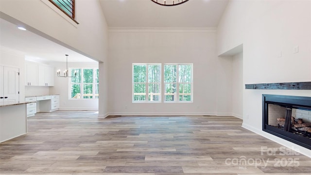 unfurnished living room featuring a fireplace, an inviting chandelier, a high ceiling, baseboards, and light wood-style floors