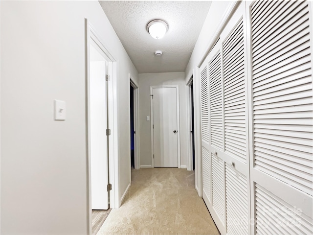 hallway with light carpet and a textured ceiling