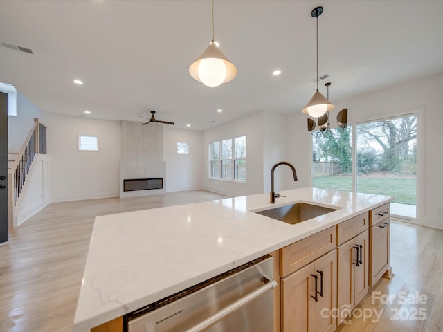 kitchen with sink, stainless steel dishwasher, a tile fireplace, ceiling fan, and a kitchen island with sink