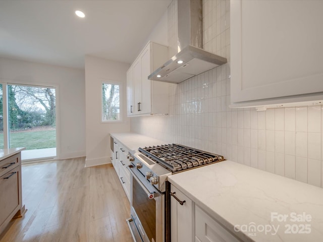 kitchen featuring white cabinetry, high end range, wall chimney range hood, light hardwood / wood-style floors, and backsplash