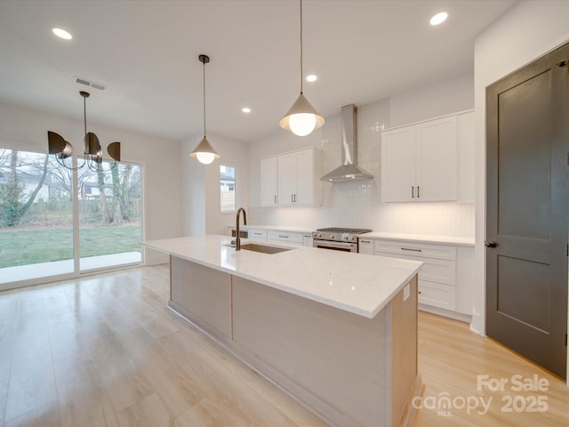 kitchen with sink, high end range, hanging light fixtures, a kitchen island with sink, and wall chimney range hood