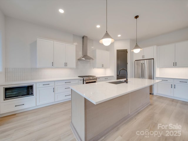 kitchen featuring sink, a kitchen island with sink, hanging light fixtures, high end appliances, and wall chimney exhaust hood