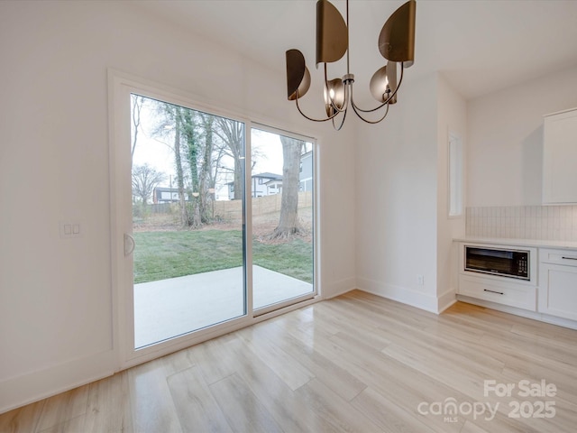 unfurnished dining area featuring plenty of natural light, an inviting chandelier, and light hardwood / wood-style flooring