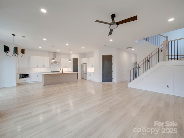 unfurnished living room with sink, ceiling fan with notable chandelier, and light wood-type flooring