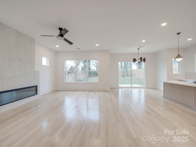 unfurnished living room with a tiled fireplace, ceiling fan with notable chandelier, and light hardwood / wood-style flooring