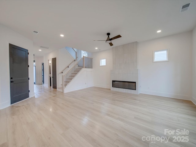 unfurnished living room with ceiling fan, a healthy amount of sunlight, a tiled fireplace, and light wood-type flooring