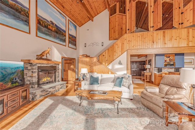 living room with wood ceiling, light hardwood / wood-style flooring, high vaulted ceiling, and a stone fireplace