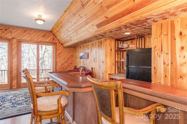 bar featuring lofted ceiling, black fridge, wood ceiling, wooden walls, and hardwood / wood-style floors