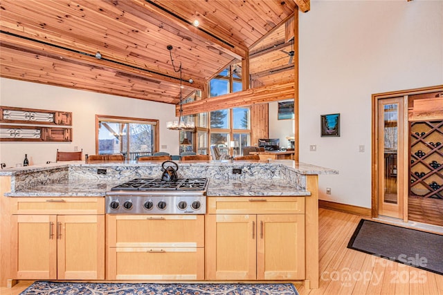 kitchen with light stone counters, stainless steel gas stovetop, kitchen peninsula, and light brown cabinets