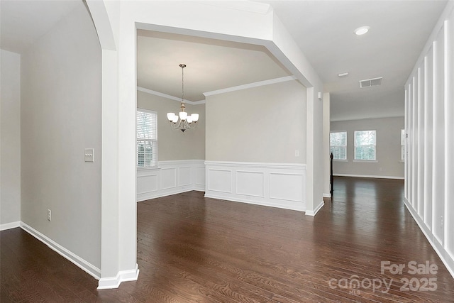 spare room with ornamental molding, a healthy amount of sunlight, dark hardwood / wood-style floors, and a chandelier