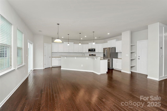 kitchen with appliances with stainless steel finishes, pendant lighting, white cabinets, a kitchen bar, and a kitchen island with sink