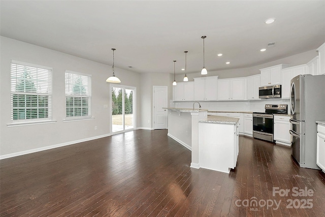 kitchen featuring white cabinetry, hanging light fixtures, stainless steel appliances, light stone countertops, and a kitchen island with sink