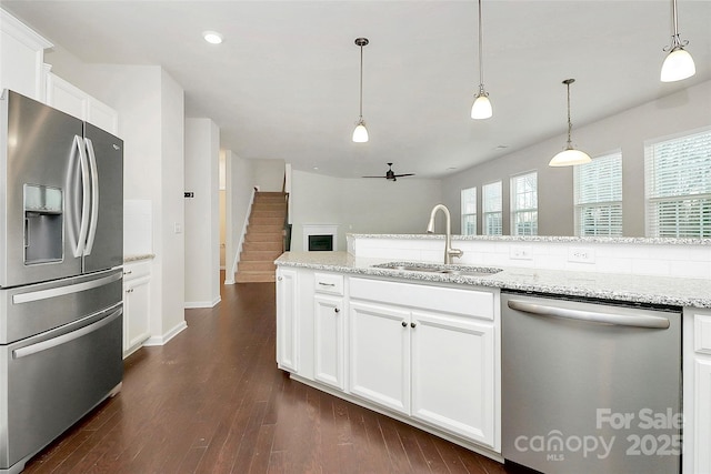 kitchen with appliances with stainless steel finishes, pendant lighting, white cabinetry, sink, and light stone counters