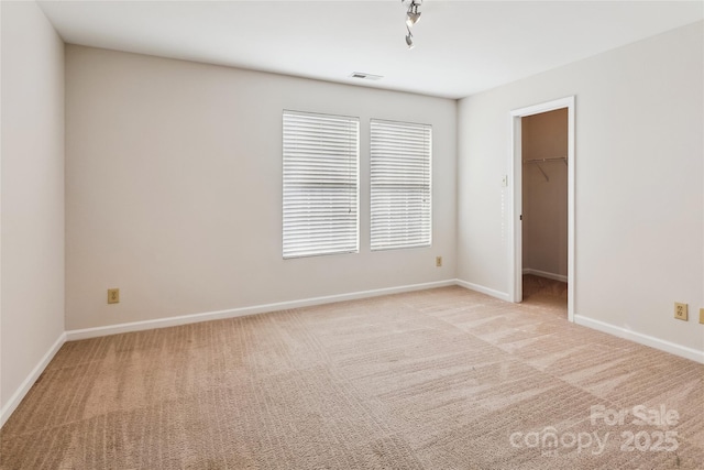 unfurnished bedroom featuring a spacious closet, light carpet, track lighting, and a closet