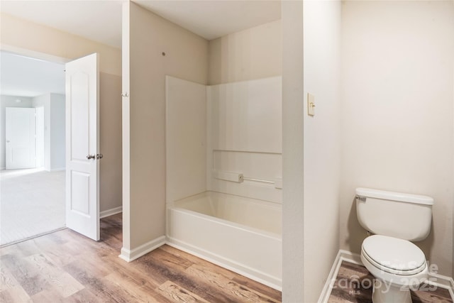 bathroom with hardwood / wood-style flooring, shower / washtub combination, and toilet