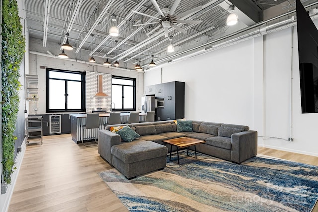 living room featuring sink, beverage cooler, a high ceiling, ceiling fan, and light wood-type flooring