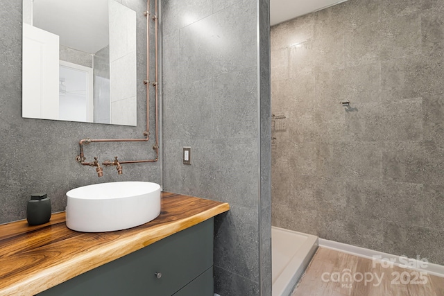 bathroom with tiled shower, vanity, and tile walls