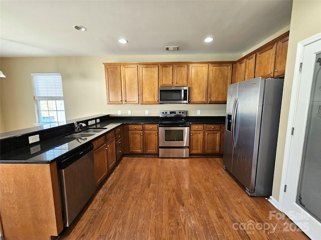 kitchen featuring visible vents, dark wood-style flooring, a sink, stainless steel appliances, and brown cabinets