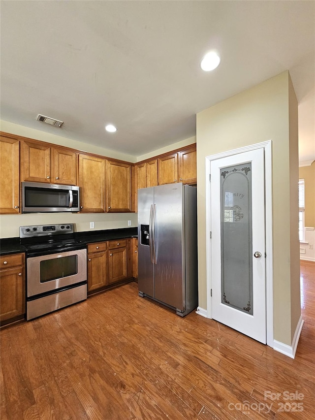 kitchen with dark countertops, appliances with stainless steel finishes, dark wood-style flooring, and brown cabinetry