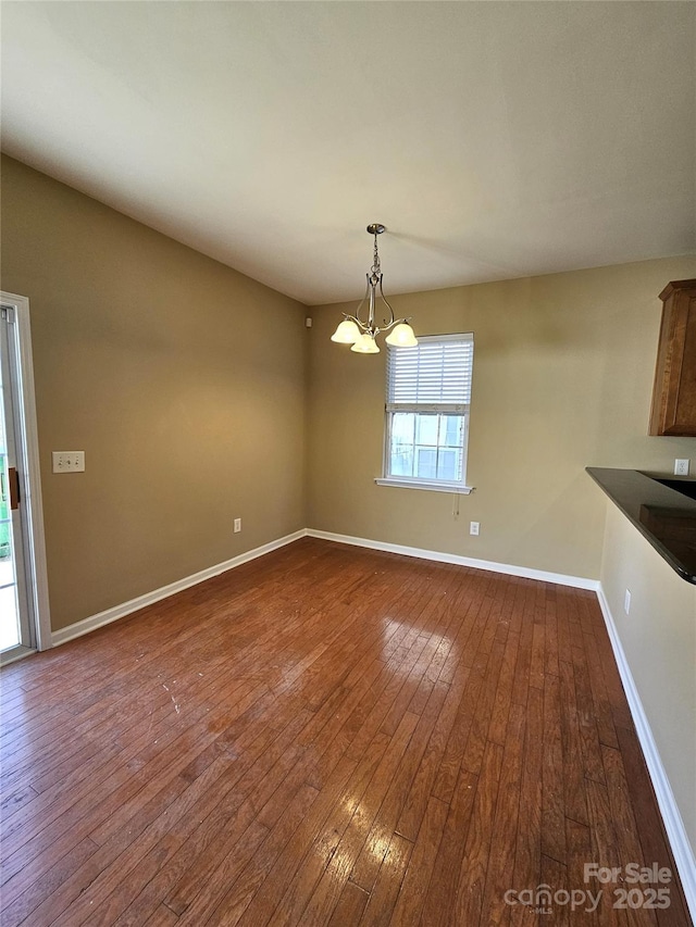 unfurnished dining area with baseboards, dark wood-style flooring, and a chandelier