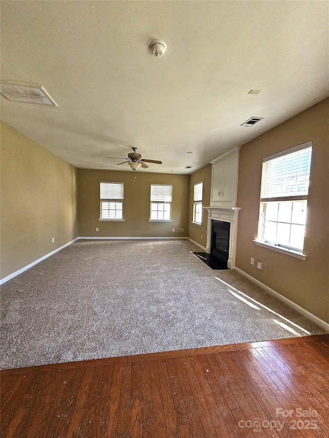 unfurnished living room featuring visible vents, a fireplace with flush hearth, baseboards, and wood-type flooring