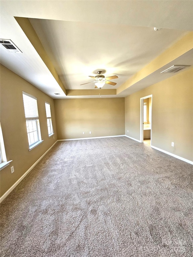 carpeted empty room with visible vents, a raised ceiling, baseboards, and ceiling fan