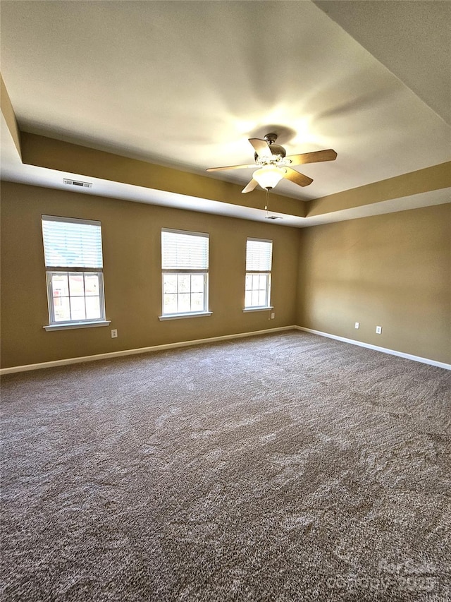 unfurnished room with carpet, baseboards, visible vents, a ceiling fan, and a tray ceiling