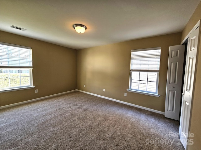 spare room with a wealth of natural light, visible vents, baseboards, and carpet