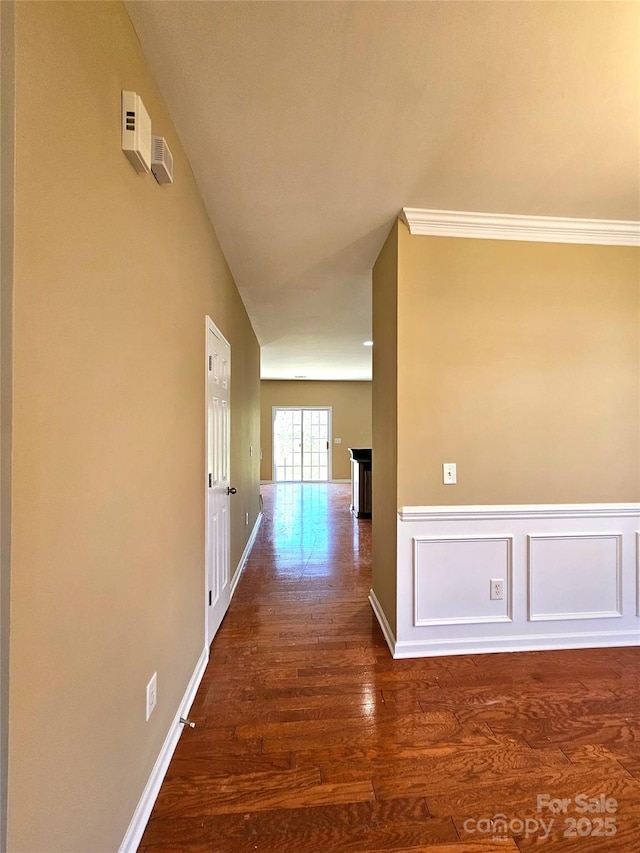 corridor featuring dark wood-type flooring, a decorative wall, and a wainscoted wall