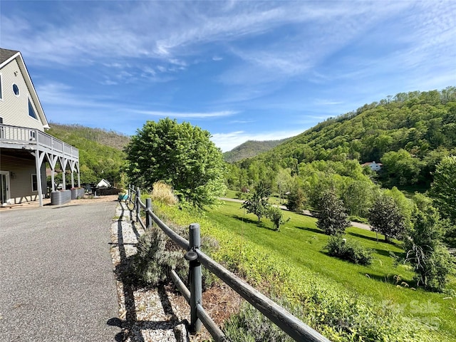 view of yard featuring a view of trees, a deck with mountain view, and fence