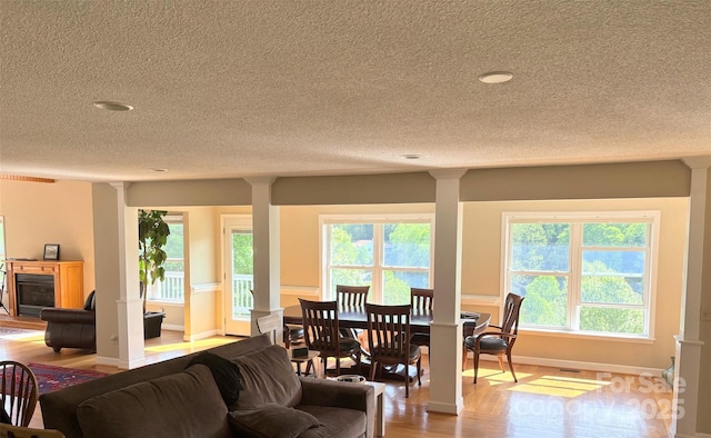 dining area featuring ornate columns, baseboards, a textured ceiling, and wood finished floors