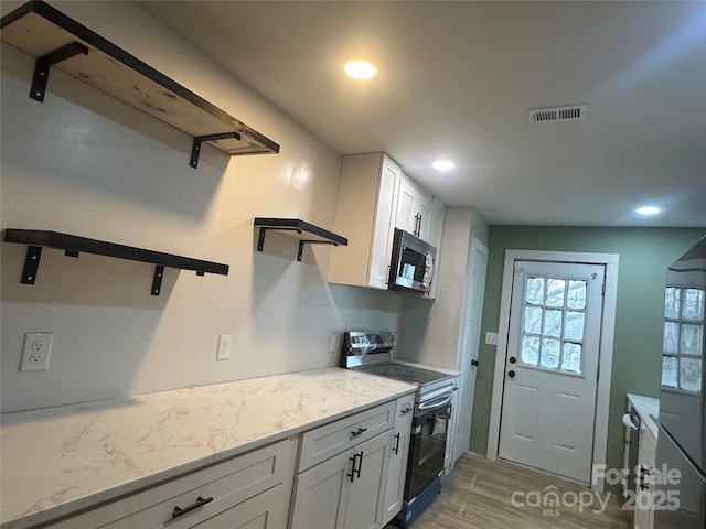 kitchen with stainless steel appliances, white cabinets, light stone counters, and light hardwood / wood-style flooring