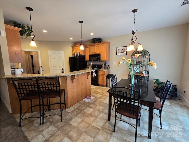 kitchen featuring hanging light fixtures, backsplash, black appliances, a kitchen bar, and kitchen peninsula