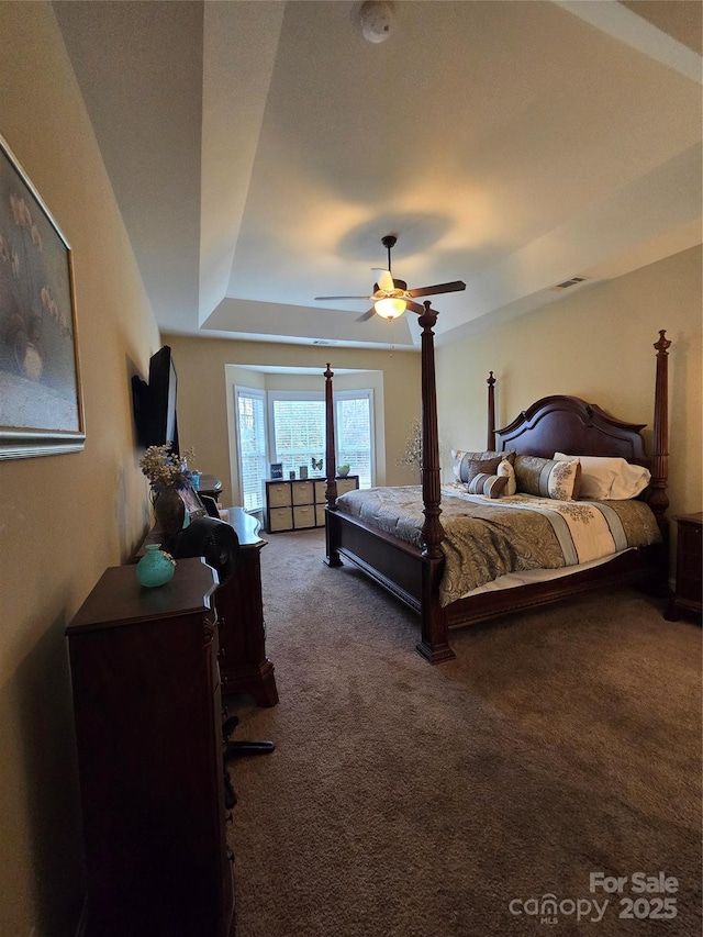 bedroom with ceiling fan, a raised ceiling, and dark carpet