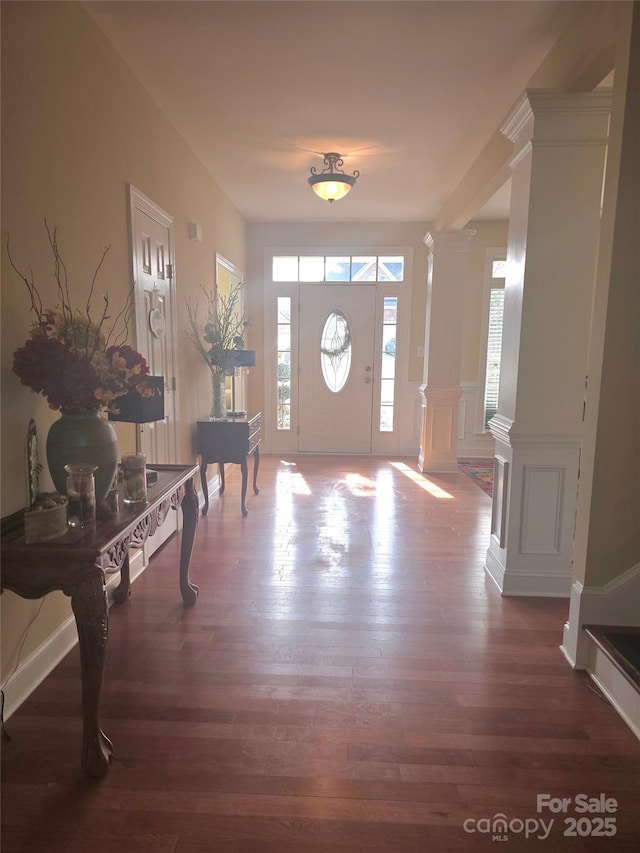 foyer entrance featuring a decorative wall, wood finished floors, and decorative columns