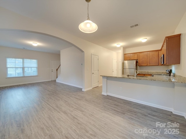 kitchen featuring appliances with stainless steel finishes, decorative light fixtures, hardwood / wood-style flooring, kitchen peninsula, and light stone countertops