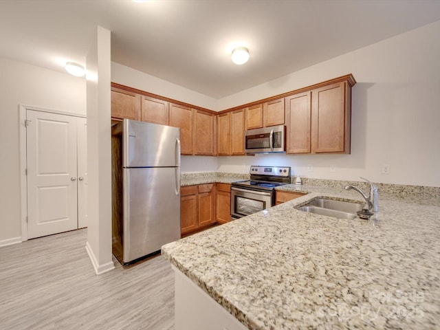 kitchen featuring appliances with stainless steel finishes, sink, kitchen peninsula, light stone countertops, and light wood-type flooring