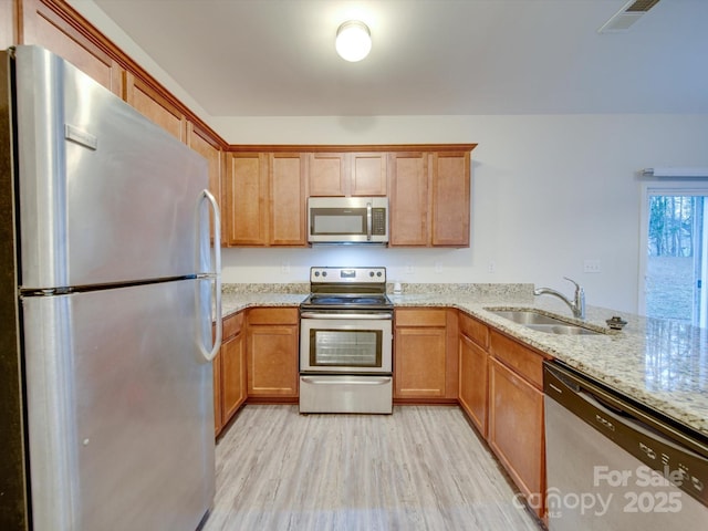 kitchen featuring sink, light wood-type flooring, appliances with stainless steel finishes, kitchen peninsula, and light stone countertops