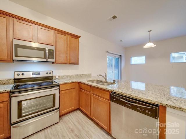 kitchen with sink, light stone counters, decorative light fixtures, appliances with stainless steel finishes, and light hardwood / wood-style floors