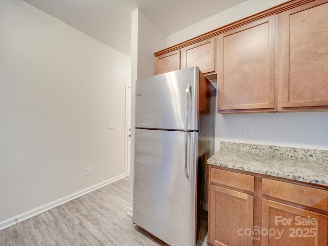 kitchen with light stone countertops, light wood-type flooring, and stainless steel refrigerator