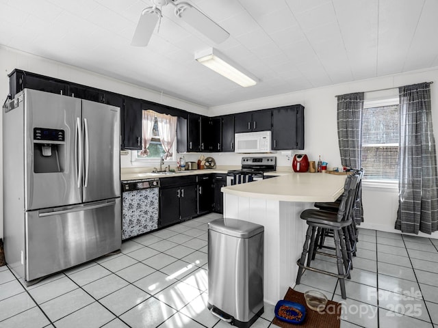 kitchen with sink, a kitchen bar, light tile patterned floors, kitchen peninsula, and stainless steel appliances