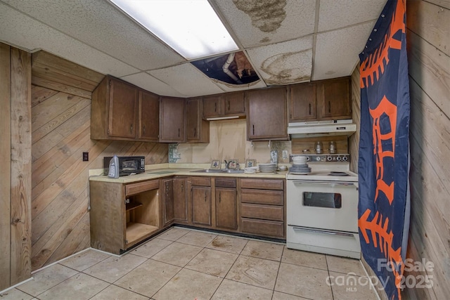 kitchen with electric stove, a drop ceiling, wood walls, light tile patterned floors, and sink