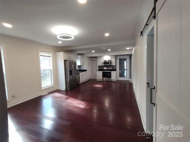 kitchen featuring crown molding, appliances with stainless steel finishes, dark hardwood / wood-style flooring, a barn door, and white cabinets