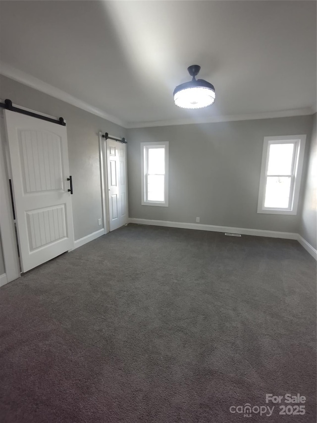 unfurnished room featuring crown molding, a barn door, and dark colored carpet