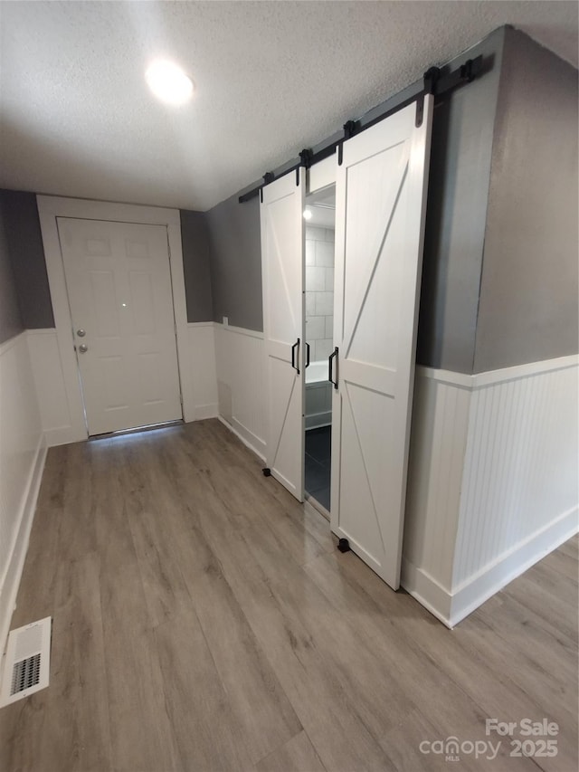 hall with a barn door, a textured ceiling, and light wood-type flooring