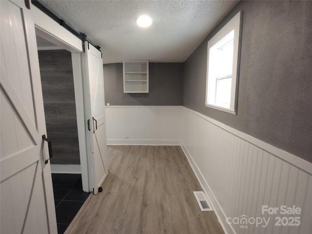 hall featuring a barn door, a textured ceiling, and light wood-type flooring