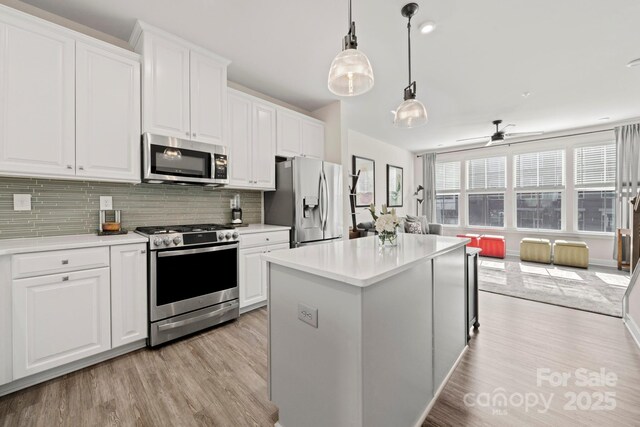 kitchen featuring decorative light fixtures, a kitchen island, stainless steel appliances, decorative backsplash, and white cabinets