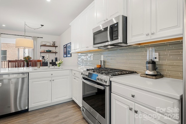 kitchen with appliances with stainless steel finishes, decorative light fixtures, sink, white cabinets, and backsplash